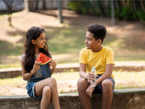 Girl and boy enjoying watermelon and bottled water in middle of discussion