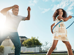 Grandfather or father figure playing with girl who is hula-hooping.