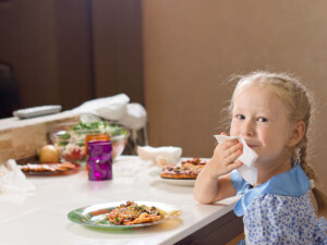 A girl at dinner table wiping her mouth and enjoying her meal