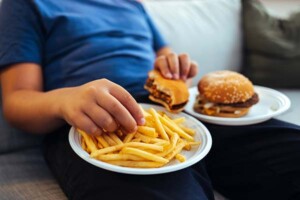 An overweight child eating two burgers and a plate of French fries