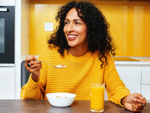 Woman eating cereal with glass of orange juice on the side.